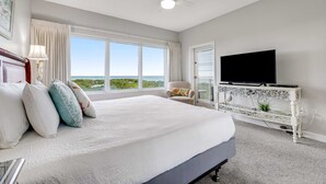 A bedroom with a large bed, a television on a white console, a ceiling fan, and a view of the outdoors. - Exclusive Gulf View 2BR with Pool Access (Miramar Beach)