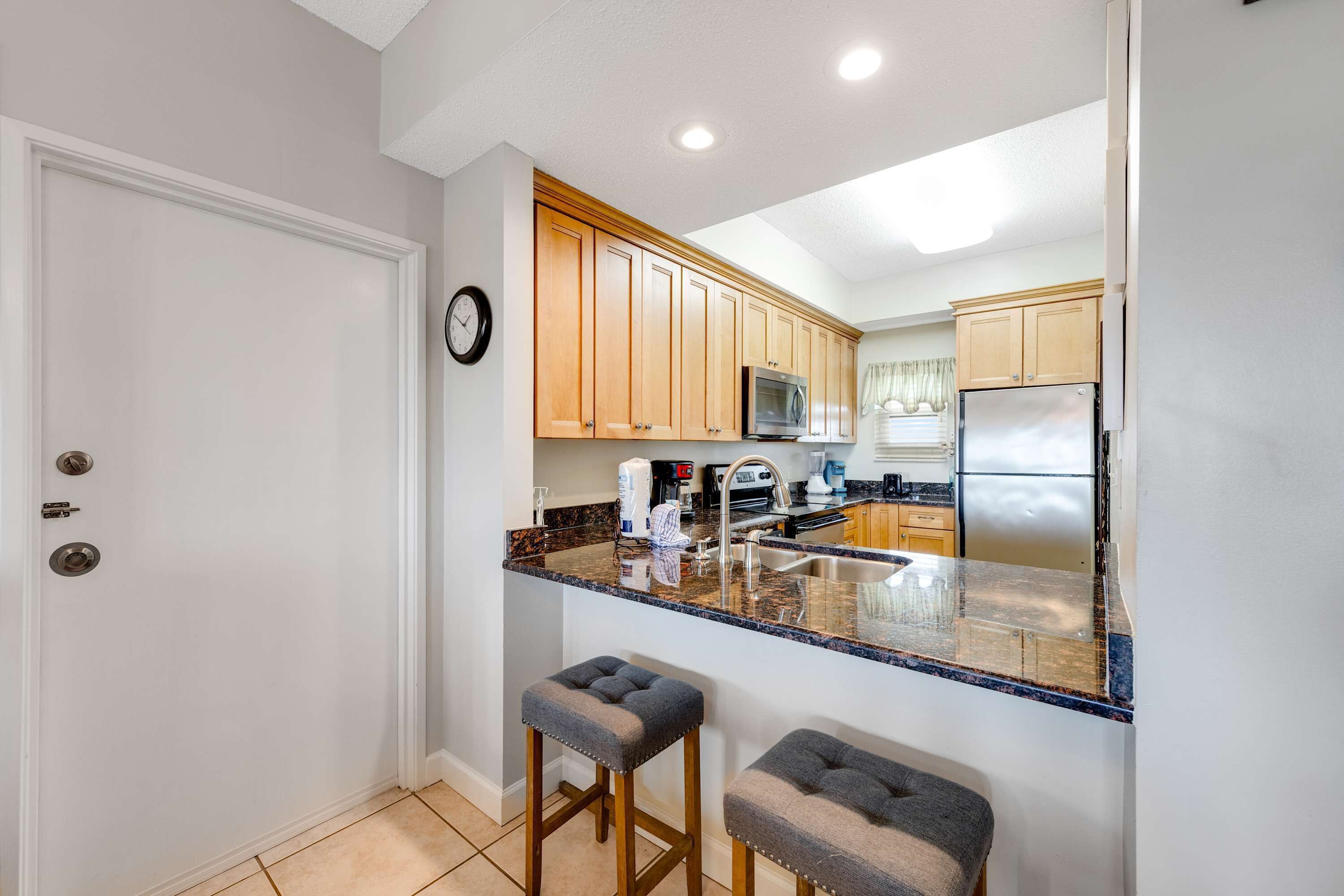 A kitchen with wooden cabinets, a stainless steel refrigerator, a microwave, and a granite countertop.