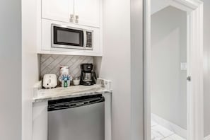 Eine kompakte Küche mit Einbau-Mikrowelle, Kaffeemaschine, Toaster und Geschirrspüler.