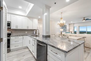 A modern kitchen with white cabinetry, a granite countertop, and a built-in dishwasher. - 2BR condo with ocean views and pool access (Miramar Beach)
