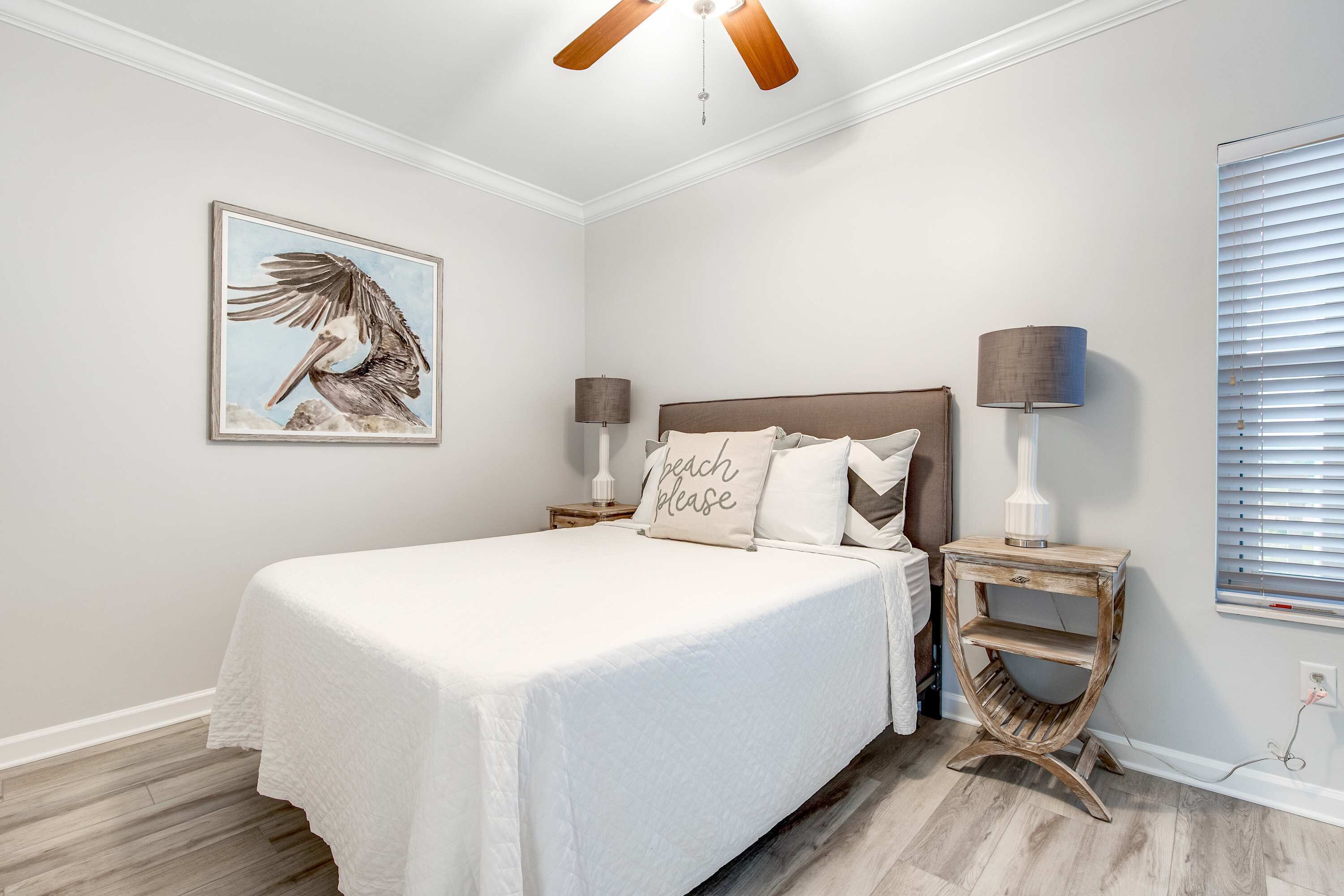 A bedroom with a bed, a nightstand, a lamp, a wall-mounted shelf, and a ceiling fan.