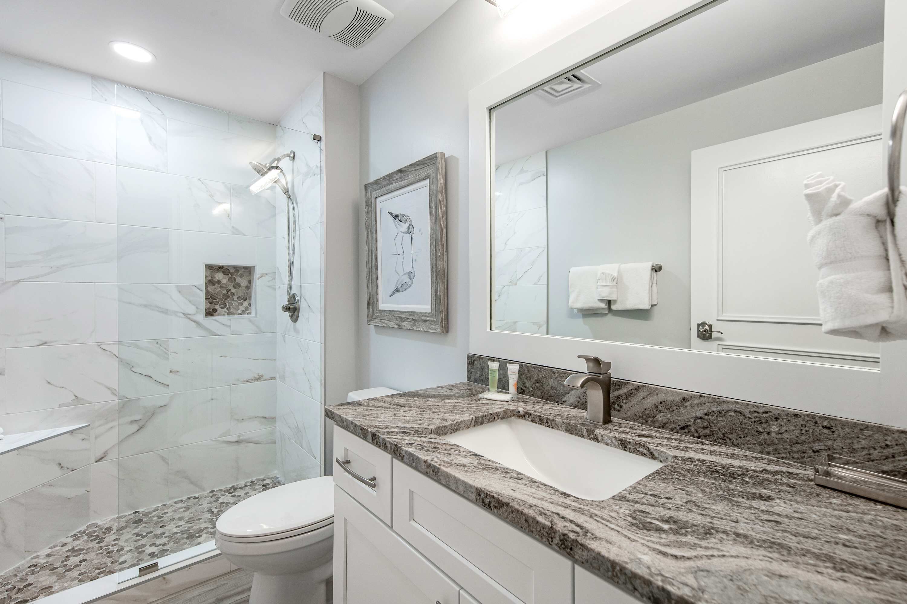 Un bagno con doccia in marmo, lavabo con specchio grande e servizi igienici.