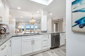 A modern kitchen with white cabinetry, a stainless steel dishwasher, and a marble countertop. - 2BR condo with ocean views and pool access (Miramar Beach)
