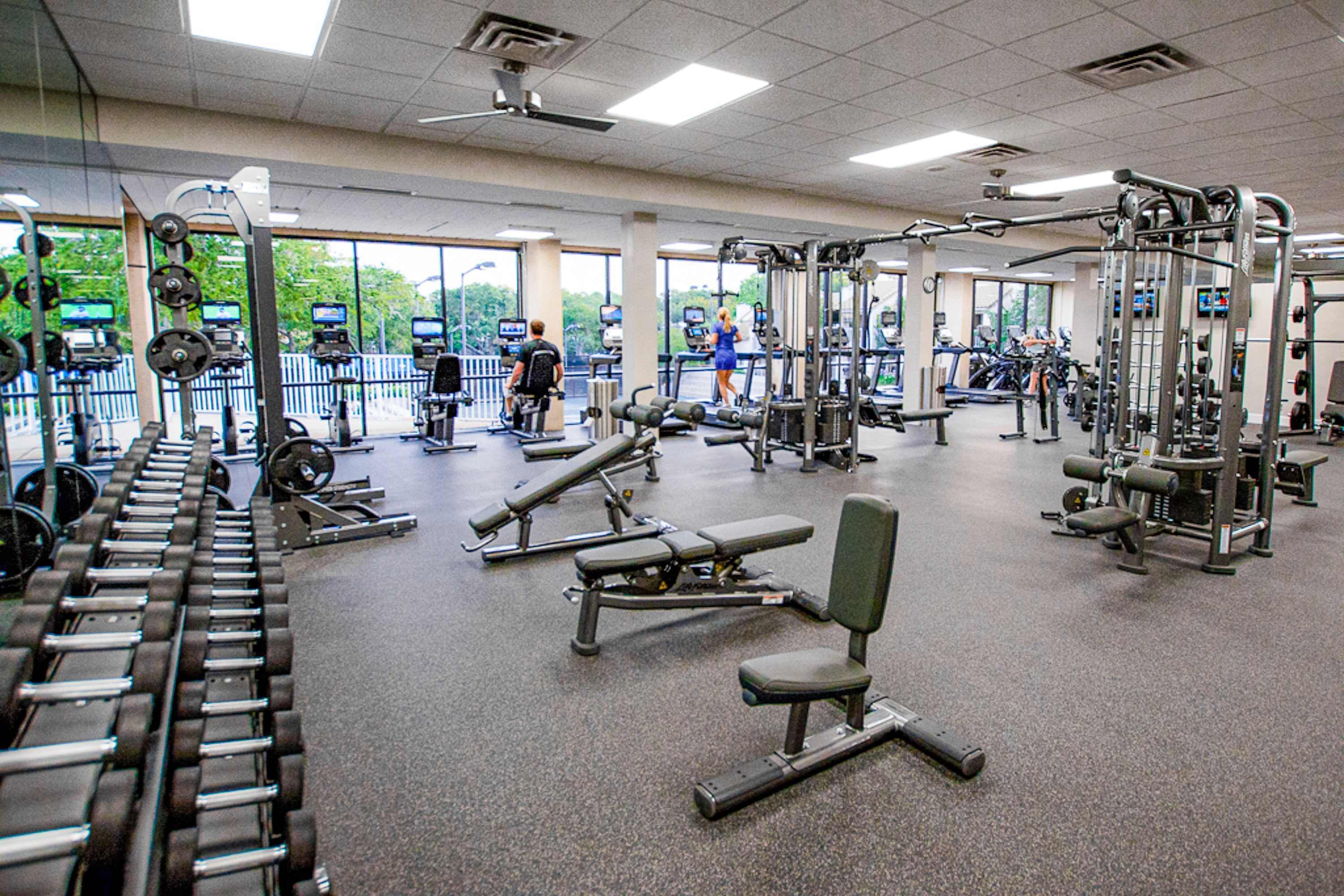 A gym with various exercise equipment, large windows, and a view of trees outside.