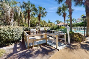 A wooden deck with barbecue grills, surrounded by palm trees and a pool. - Steps to beach, cozy retreat with pool access (Miramar Beach)