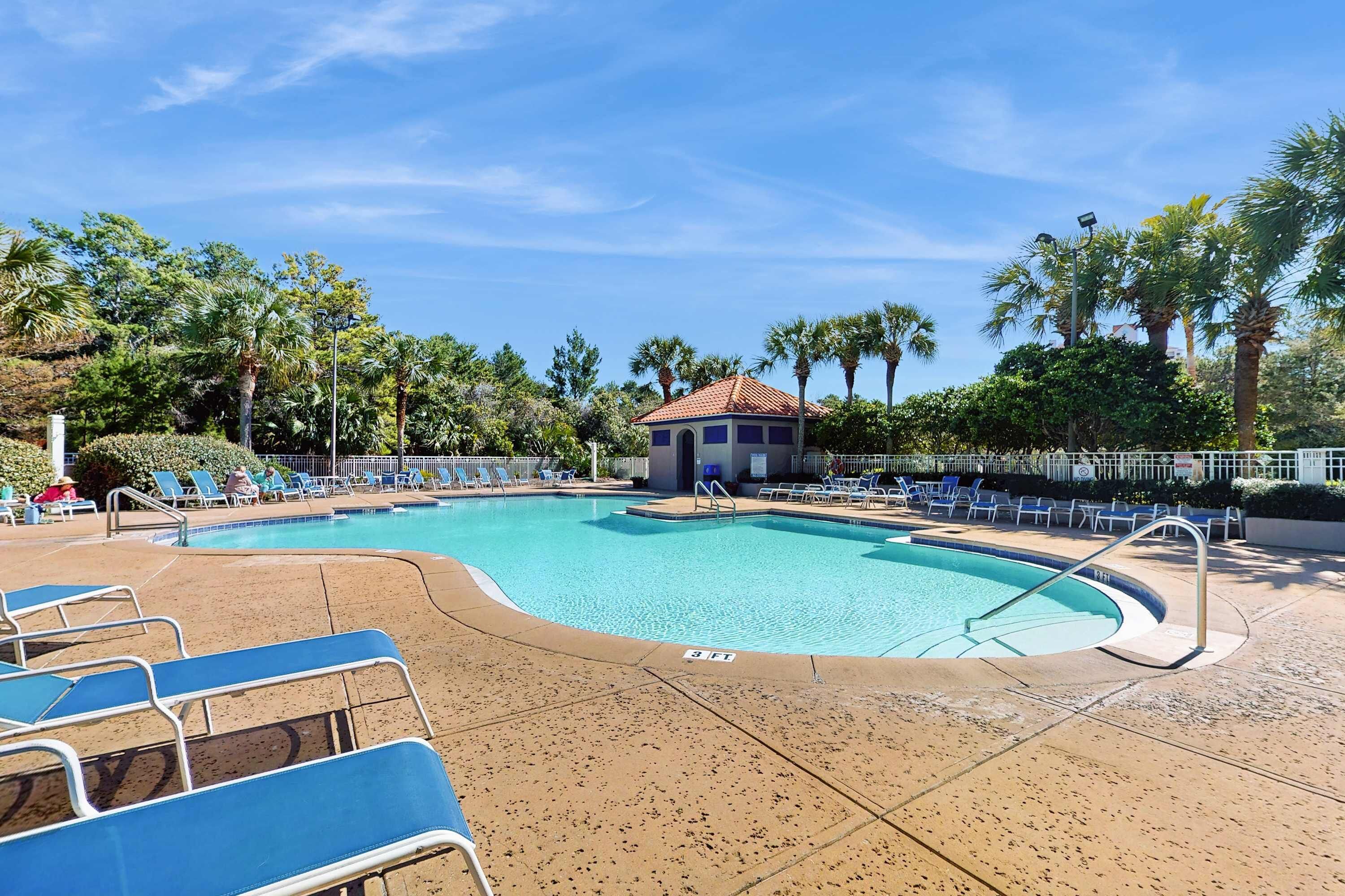 A swimming pool with lounge chairs, a small building, and palm trees.