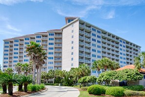 A multi-story hotel with a central courtyard, surrounded by palm trees and well-maintained landscaping. - Steps to beach, cozy retreat with pool access (Miramar Beach)