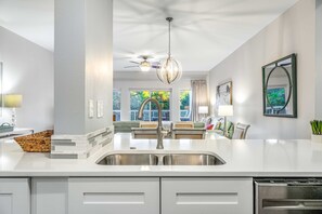 A modern kitchen with a central island, stainless steel sink, and a ceiling fan. - Exclusive 2BR condo, steps to beach & pool (Miramar Beach)