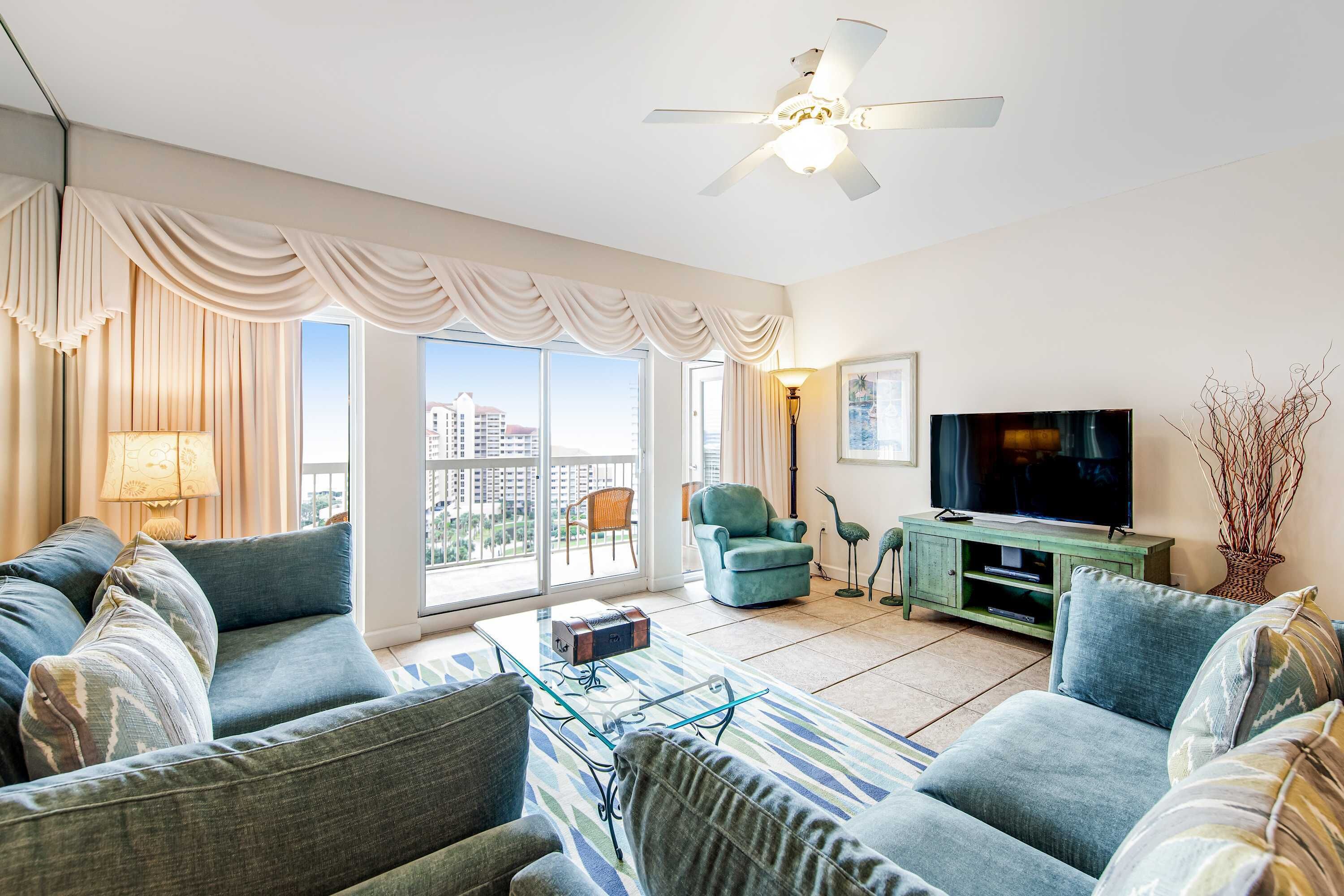 A modern living room with a sofa, armchairs, a TV, and a ceiling fan.
