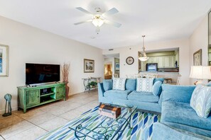 A living room with a television, sofa, coffee table, and a ceiling fan. - 2BR Gulf view, private balcony, pool access (Miramar Beach)