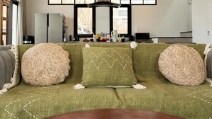 Un soggiorno con un divano verde, cuscini decorati, un tavolino in legno e una lampada a sospensione.