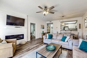 A living room with a flat-screen TV, ceiling fan, fireplace, sofa, and dining area. - 2BR Resort Condo: Balcony, Pool, Beach Access (Miramar Beach)