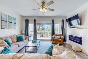 A living room with a sofa, coffee table, TV, ceiling fan, and a view to the outside. - 2BR Resort Condo: Balcony, Pool, Beach Access (Miramar Beach)