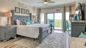 A bedroom with a bed, bedside tables, a ceiling fan, a large window, and a view of the outdoors. - Scenic balcony views & resort pool access (Miramar Beach)