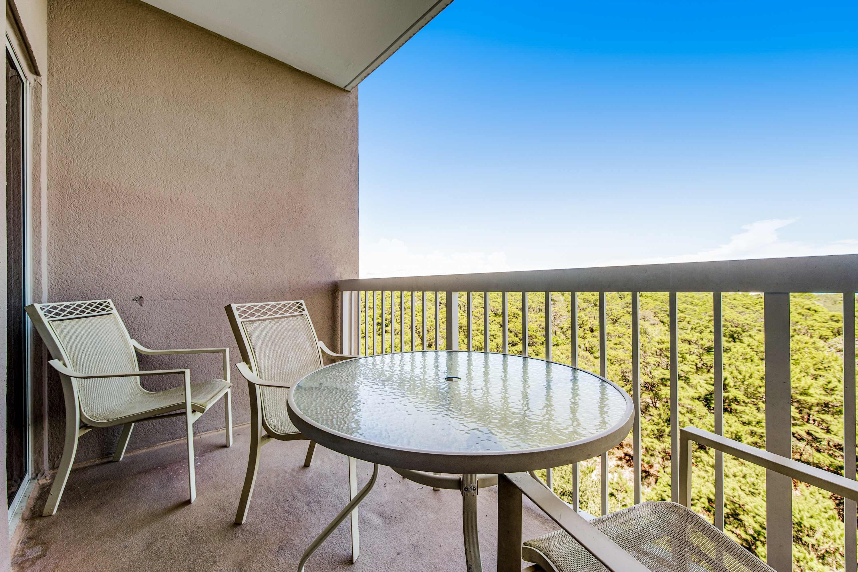 Ein Balkon mit einem runden Glastisch und zwei Stühlen mit Blick auf eine grüne Landschaft.