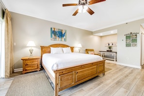A bedroom with a wooden bed, two bedside tables, a ceiling fan, and a wall with decorative items. - Exclusive studio: Gulf views, resort perks (Miramar Beach)