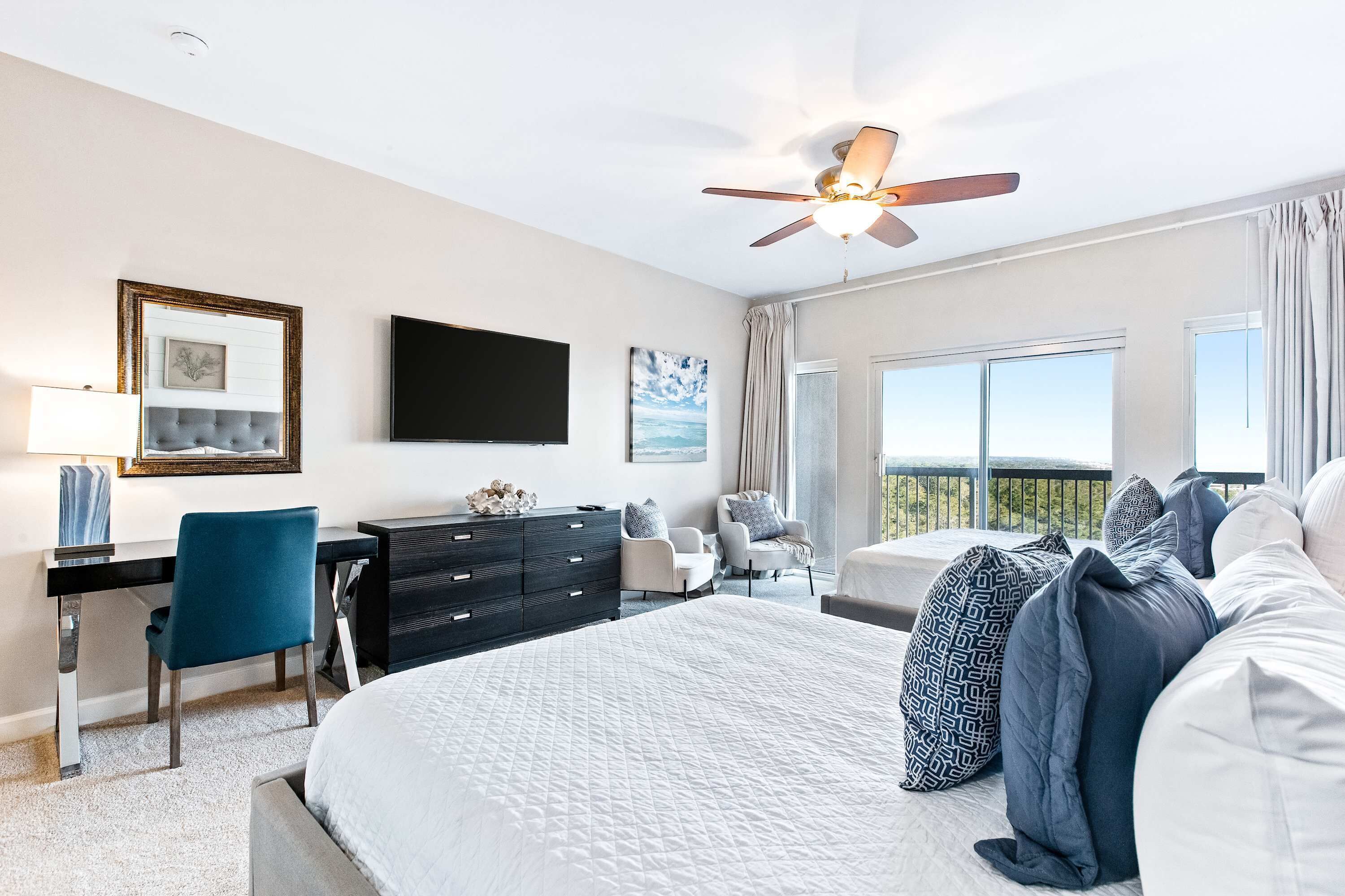 Habitación de hotel con cama, escritorio, silla, cómoda y ventilador de techo.