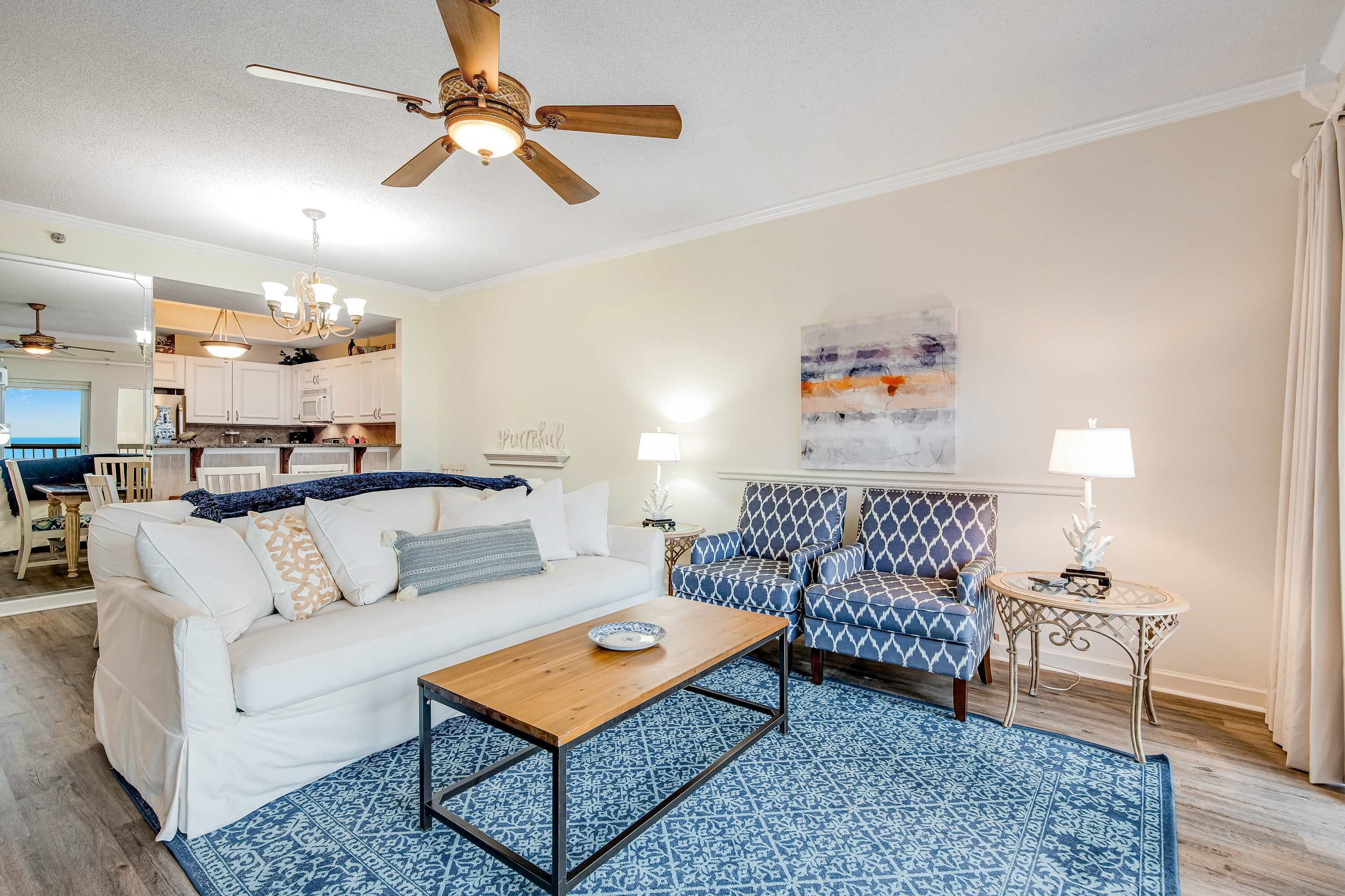 A living room with a white sofa, blue patterned rug, and a ceiling fan.
