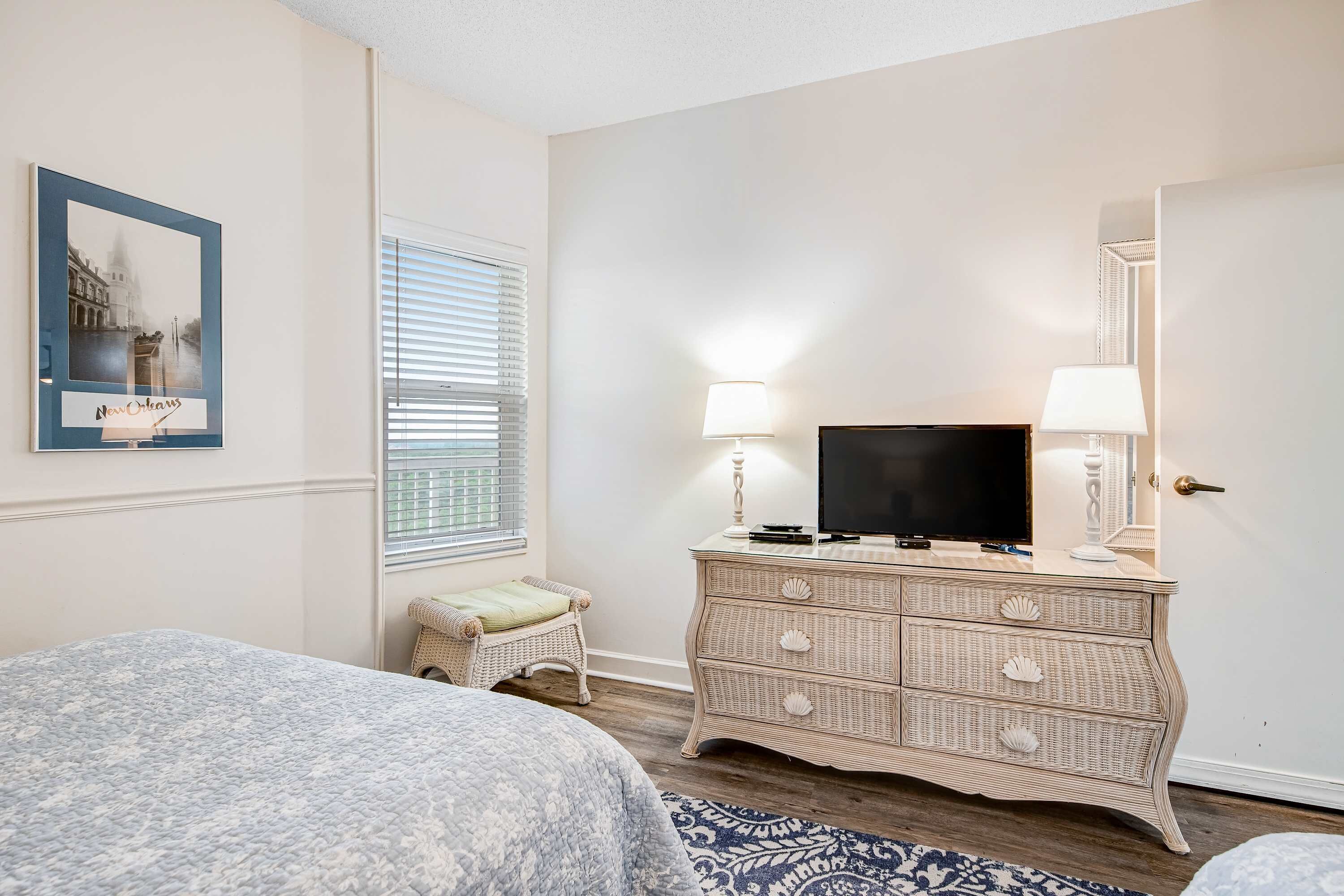 A bedroom with a bed, a dresser, a television, and a framed picture on the wall.
