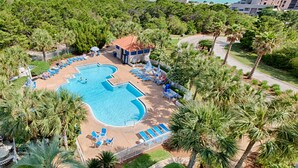 Eine Vogelperspektive zeigt ein Resort mit Schwimmbad, Liegestühlen und Palmen.