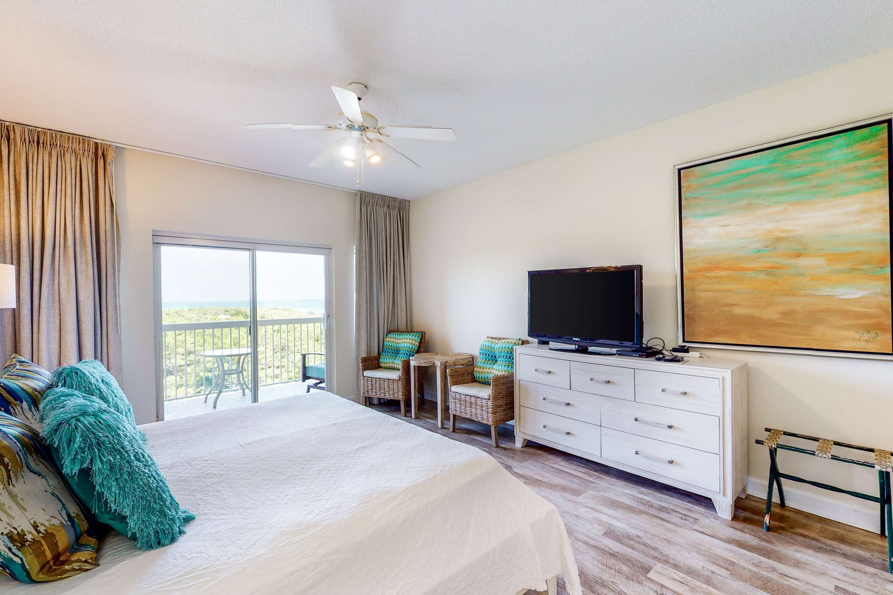 Habitación de hotel con cama, televisor, escritorio y balcón con vistas.