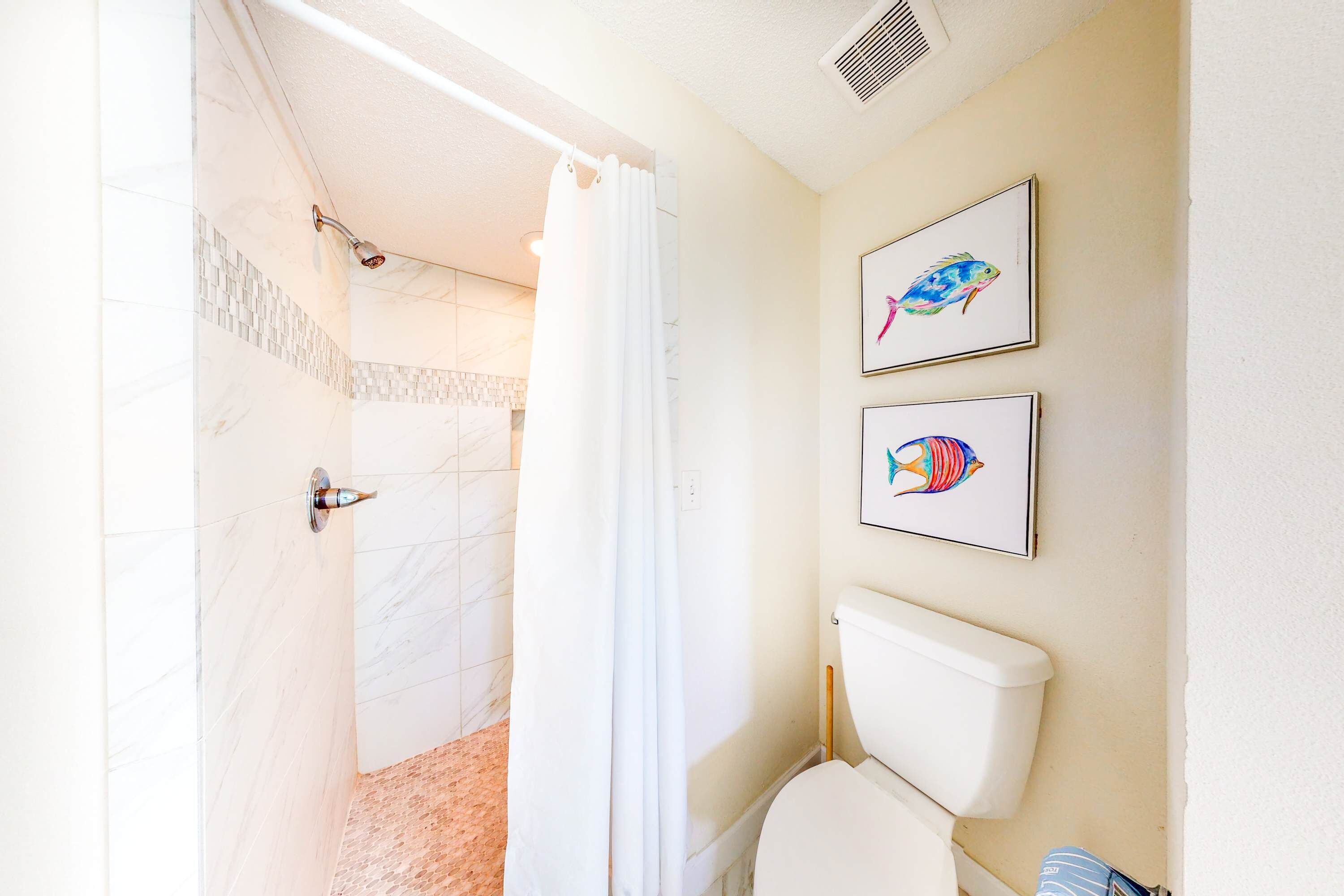 Une salle de bain avec douche, toilettes et deux tableaux représentant des poissons, encadrés et accrochés au mur.