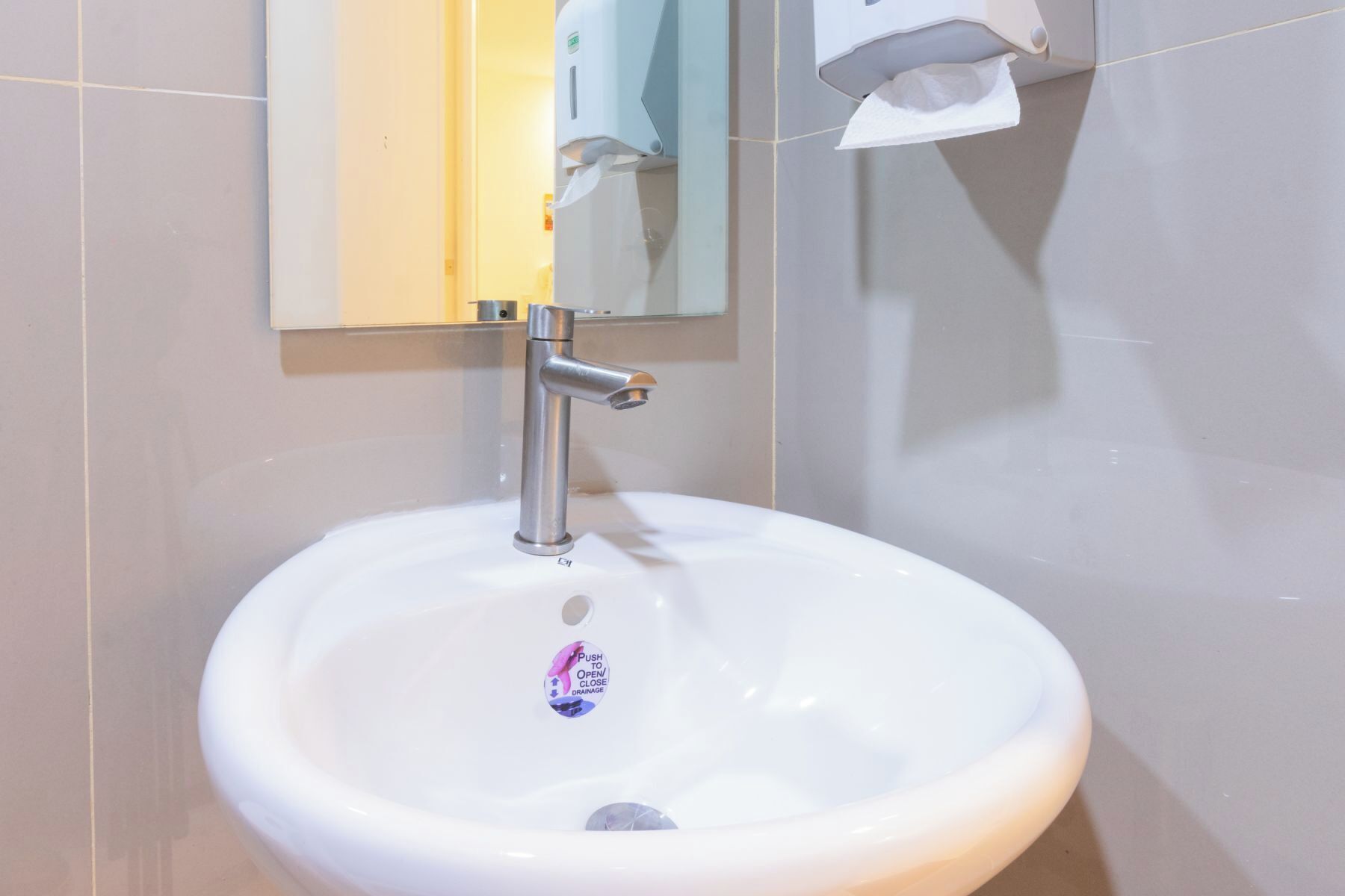 A white bathroom sink with a single faucet, a mirror above it, and a tissue dispenser on the wall.