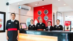 A hotel reception area with a red wall, clocks, and a menu stand. - Hotel Sogo Baliwag Bulacan (Baliuag)