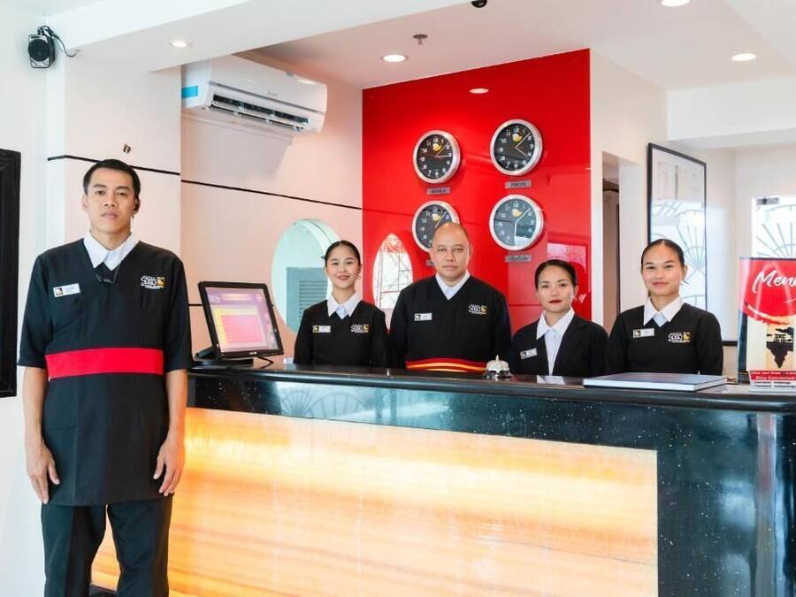 A hotel reception area with a red wall, clocks, and a menu stand.