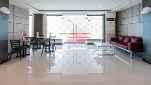 A modern lobby with a dining area, a sofa, and a large window with a view of a building. - Hotel Sogo Baliwag Bulacan (Baliuag)