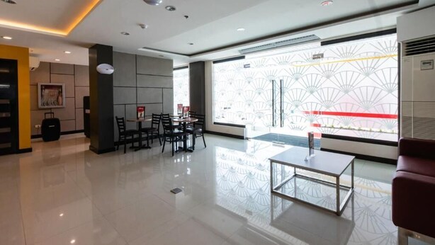 A modern hotel lobby with a seating area, a reception desk, and a large window with a view of a building with a red and white facade. - Hotel Sogo Baliwag Bulacan (Baliuag)