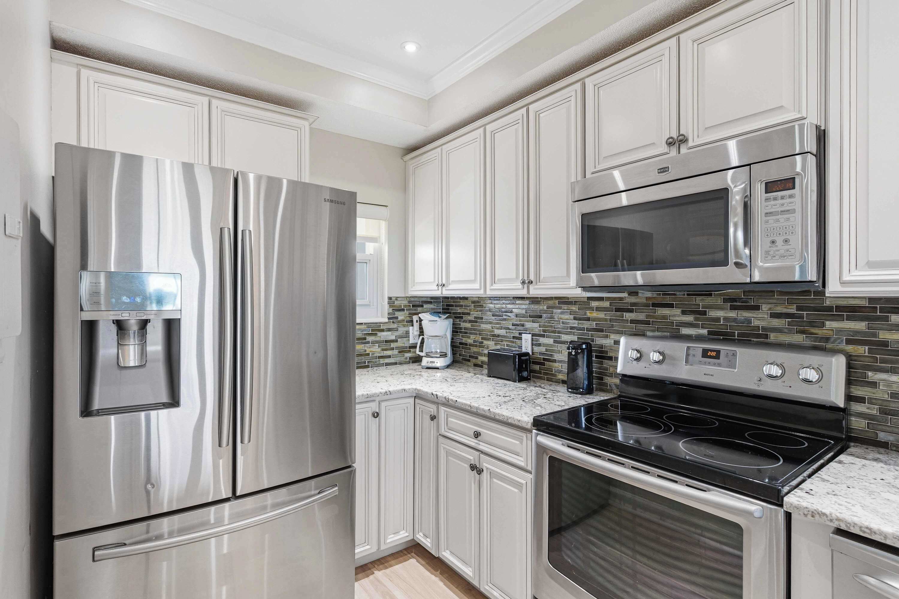 A kitchen with stainless steel appliances, white cabinetry, a tiled backsplash, and a built-in microwave.