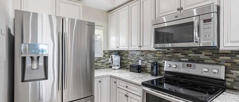 A kitchen with stainless steel appliances, white cabinetry, a tiled backsplash, and a built-in microwave.