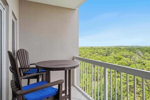 Ein Balkon mit rundem Tisch und zwei Stühlen, einem weißen Geländer und Blick auf eine grüne Landschaft.