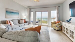 Una sala de estar con sofá, mesa de centro, sillón estampado, televisor y balcón con vistas.