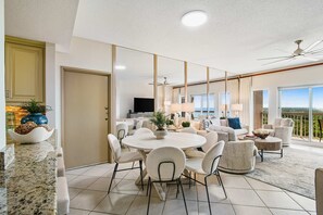 A spacious living area with a round dining table, comfortable seating, a flat-screen TV, and a balcony with a view. - Exclusive Gulf View, 2BR Balcony (Miramar Beach)