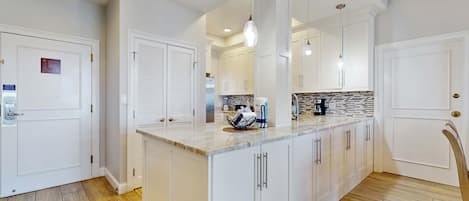 A modern kitchen with white cabinetry, a marble countertop, and pendant lighting.