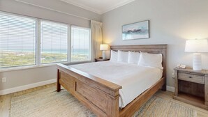 A bedroom with a large bed, a nightstand, a lamp, and a window with blinds. - Exclusive Gulf-view penthouse, sleeps 6 (Miramar Beach)