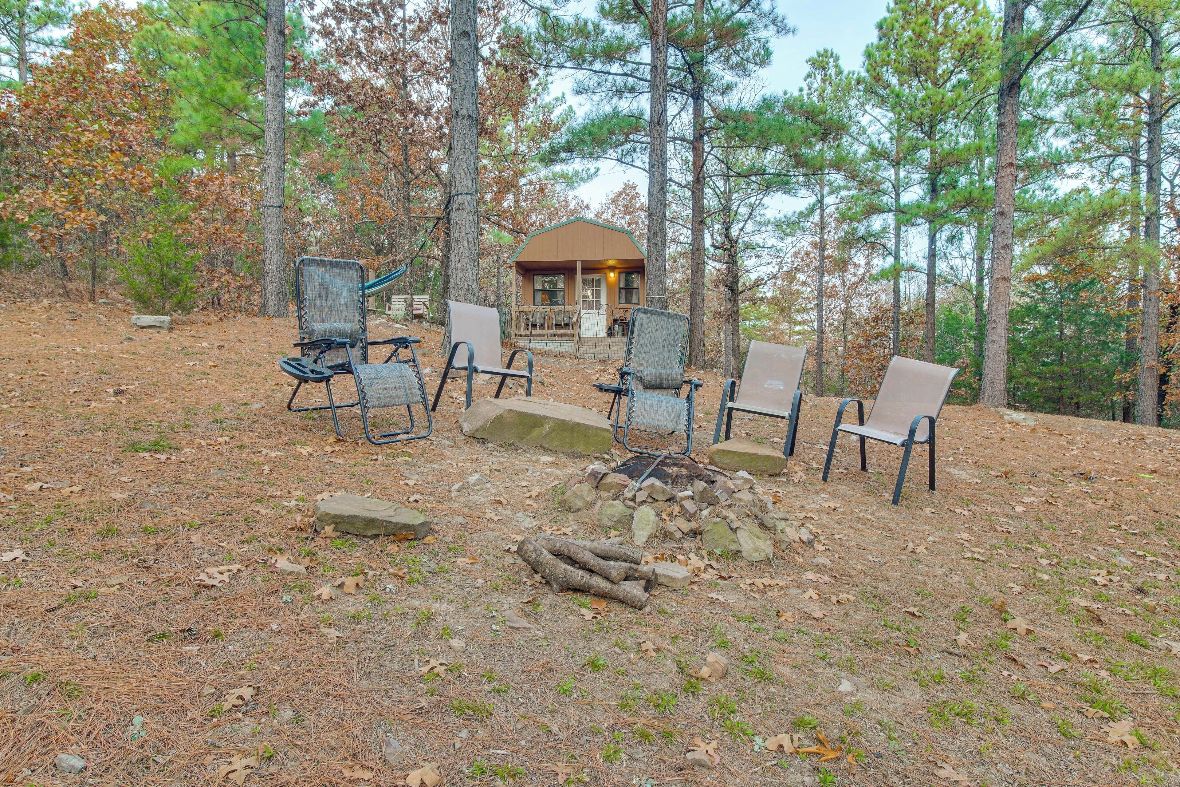 An outdoor seating area with chairs and a fire pit, surrounded by trees and a cabin in the background.