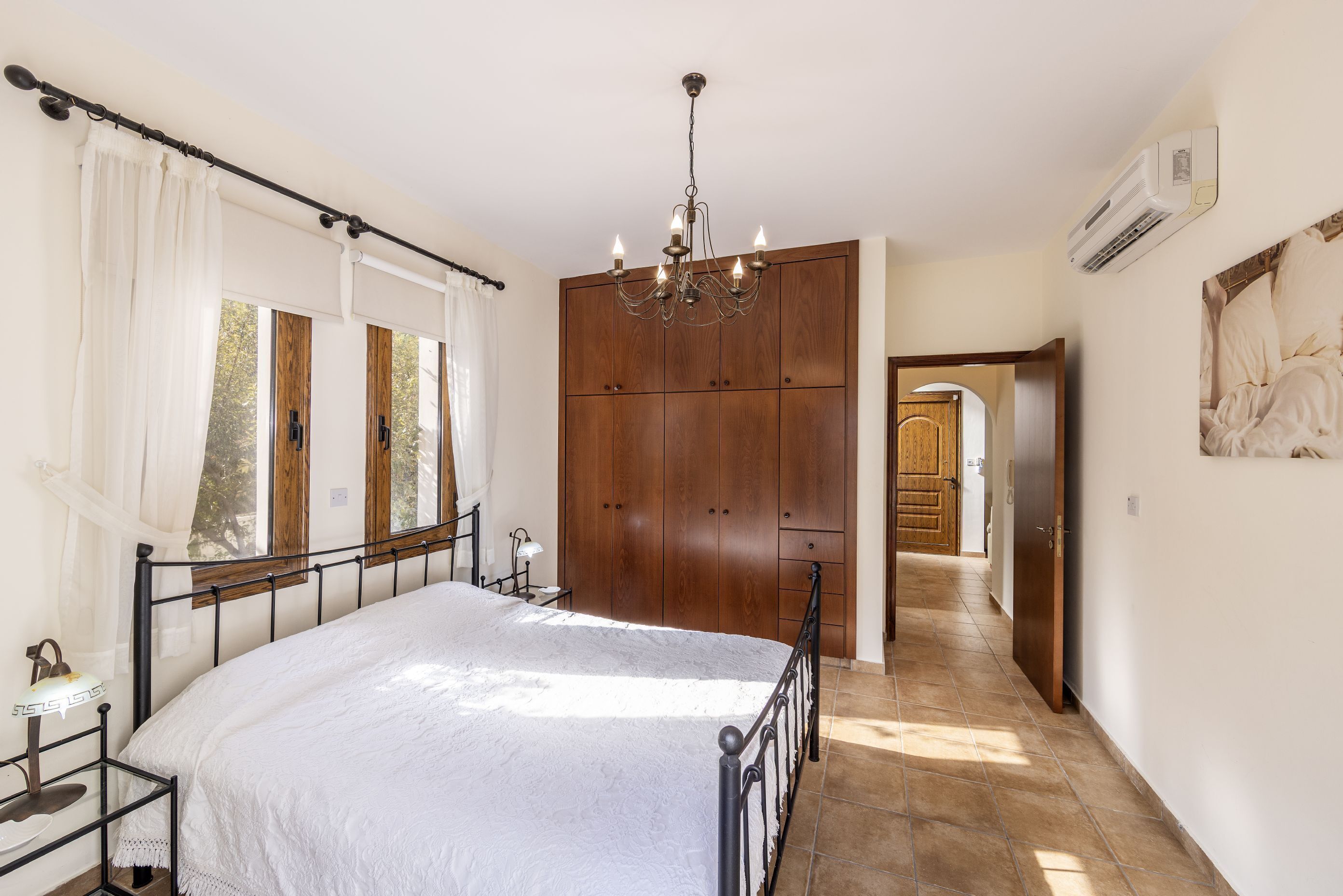 Een slaapkamer met een groot bed, een houten garderobe en een kroonluchter.