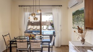 A dining area with a glass table and chairs, a view of a pool, and a painting on the wall. - Villa Relax, just steps from Latchi beach with a private pool and terraces. (Latchi Beach)