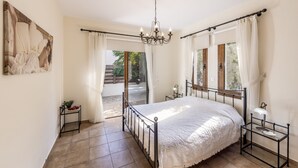 A bedroom with a large bed, a chandelier, a view of the outside, and a painting on the wall. - Villa Relax, just steps from Latchi beach with a private pool and terraces. (Latchi Beach)