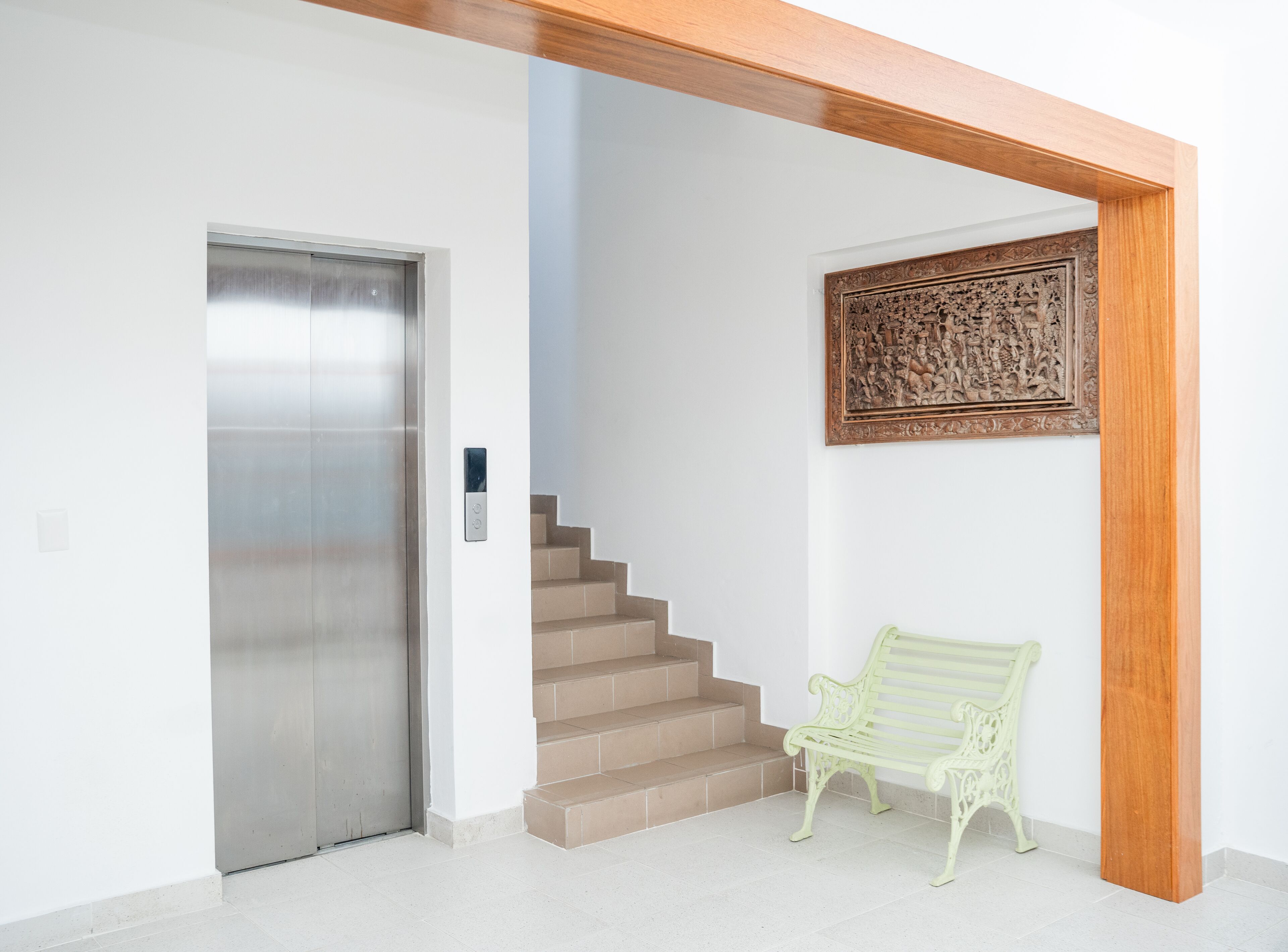 A modern interior with a metallic elevator, a staircase, and a green bench.