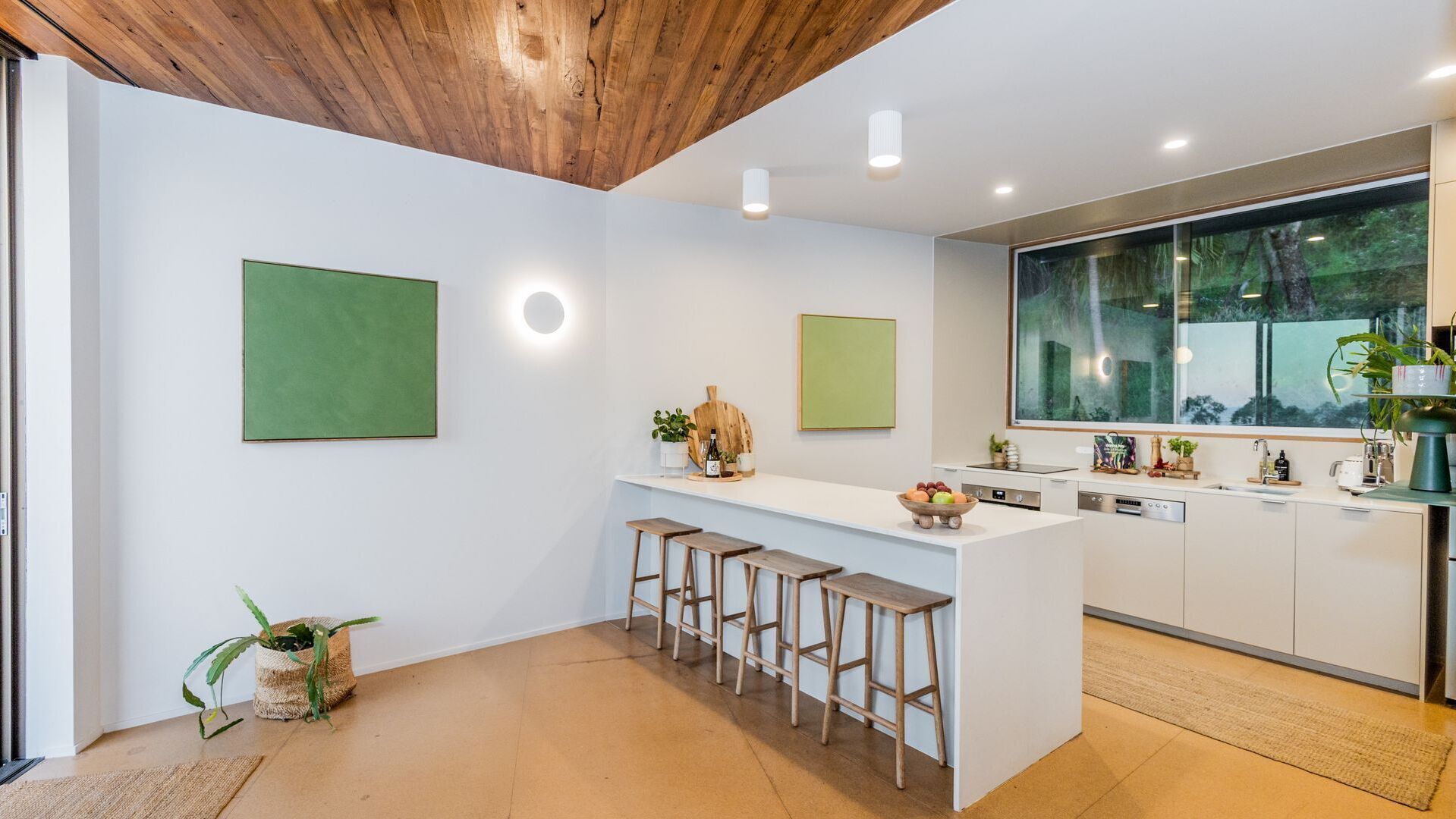 Une cuisine moderne avec un plafond en bois, des armoires blanches, une grande fenêtre et un îlot central doté de tabourets.