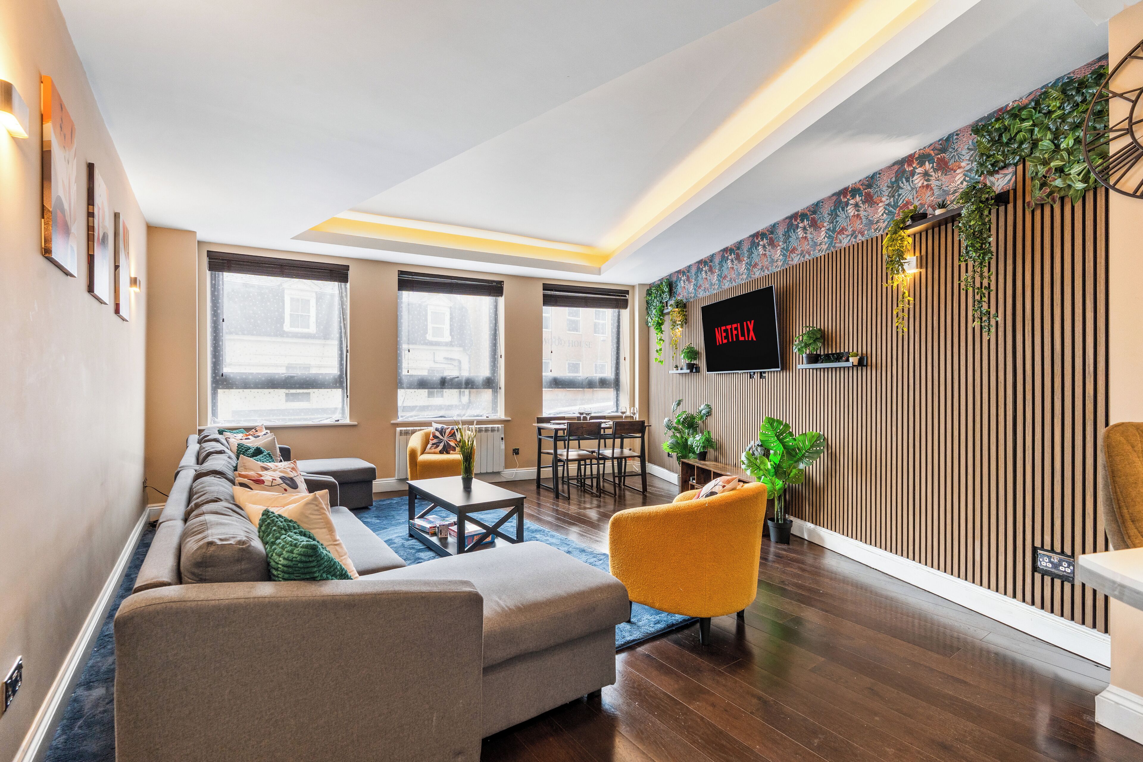 Ein modernes Wohnzimmer mit einer Couch, Sesseln, einem Couchtisch und einem an einer Holzwand montierten Fernseher.