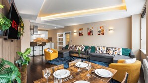 Una sala de estar moderna con comedor, un conjunto de sofás y una cocina al fondo.