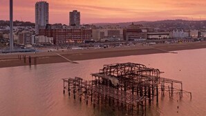 Un paisaje urbano costero al atardecer con un muelle prominente en primer plano.