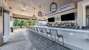 A bar area with a long counter, multiple bar stools, ceiling fans, and a TV screen. - Private River Strand pool home with golf membership - Villa Milano (Bradenton)