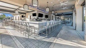 An outdoor bar area with a long counter, multiple bar stools, and hanging pendant lights. - Private River Strand pool home with golf membership - Villa Milano (Bradenton)
