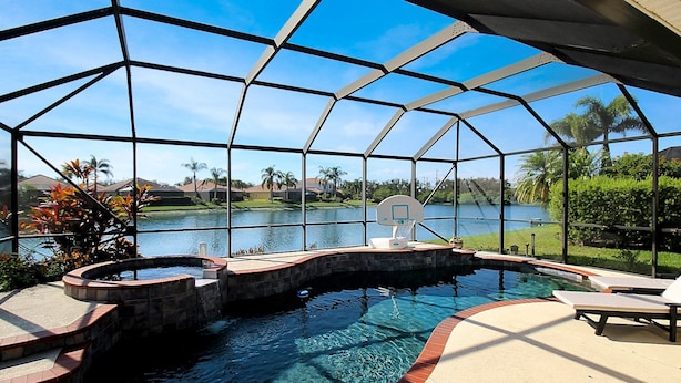 A swimming pool with a hot tub, surrounded by a covered patio with a view of a lake and palm trees. - Private River Strand pool home with golf membership - Villa Milano (Bradenton)